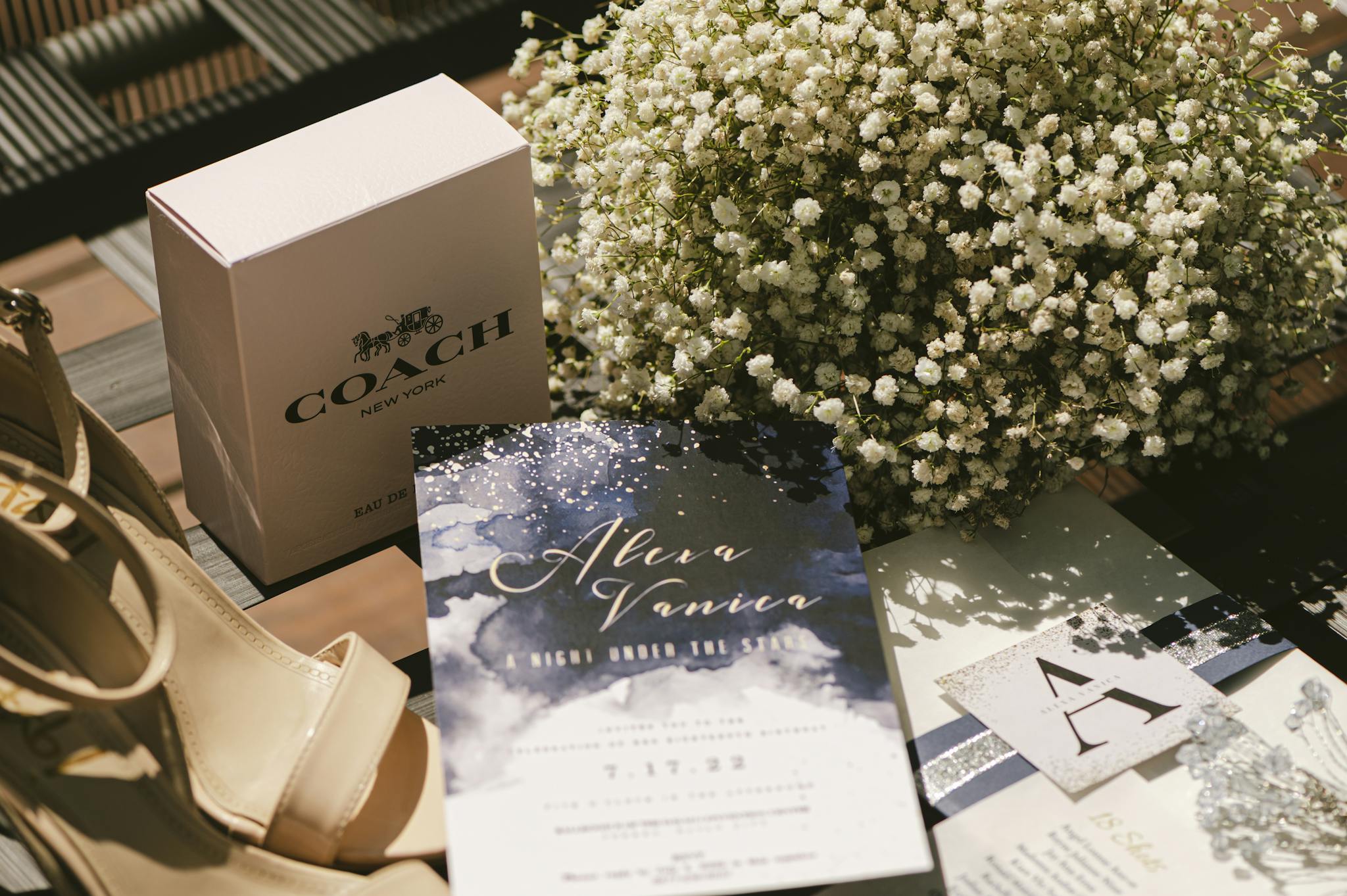 A stylish wedding invitation set with shoes, luxury perfume, and flowers.